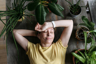 Woman with eyes closed relaxing amidst plants at home - VYF00960