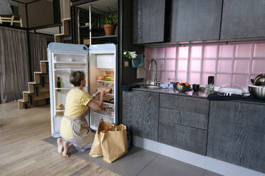 Woman stocking groceries in fridge at home - VYF00974
