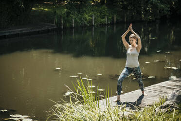Frau, die an einem sonnigen Tag auf einem Steg in der Nähe des Sees trainiert - MJRF00947