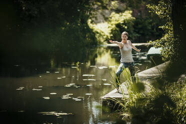 Woman practicing yoga on pier near lake - MJRF00948