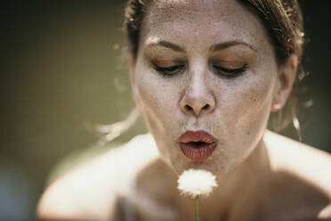 Mature woman blowing dandelion on sunny day - MJRF00952