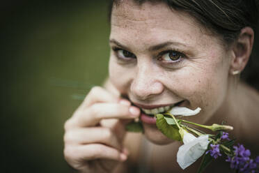 Smiling woman holding flowers in mouth - MJRF00955