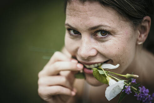 Lächelnde Frau mit Blumen im Mund - MJRF00955