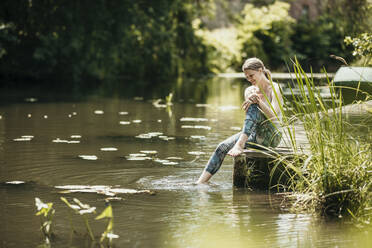 Frau taucht Bein ins Wasser und sitzt am See - MJRF00956