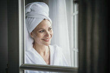 Lächelnde reife Frau mit Handtuch auf dem Kopf zu Hause - MJRF00972