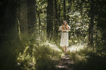 Woman with hands clasped standing in forest - MJRF00975