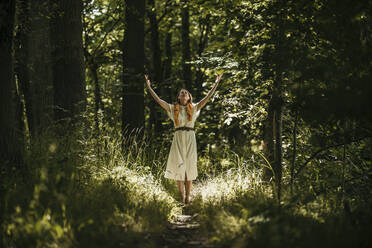 Woman with arms raised standing in forest - MJRF00976
