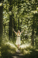 Woman with hands raised standing in forest at sunny day - MJRF00977