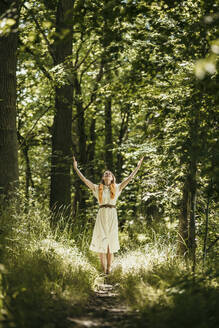 Frau mit erhobenen Händen stehend im Wald an einem sonnigen Tag - MJRF00977