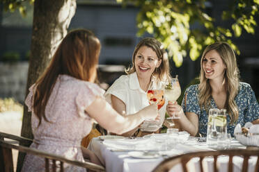 Happy female friends toasting drinks sitting at table in restaurant - MJRF00985