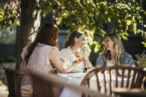 Happy friends enjoying drinks at dining table in restaurant - MJRF00986