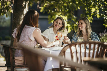 Lächelnde Frauen, die am Esstisch im Restaurant sitzen und Getränke genießen - MJRF00987