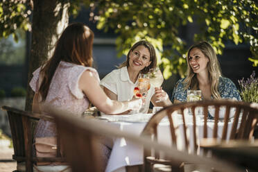 Smiling women enjoying drinks sitting at dining table in restaurant - MJRF00987