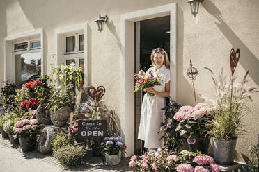 Ältere Frau mit Blumen steht in der Nähe der Tür eines Blumenladens - MJRF00995