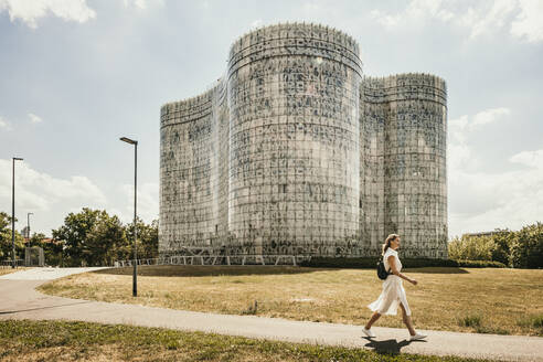 Woman walking on footpath in front of library at sunny day in Cottbus, Germany - MJRF01000