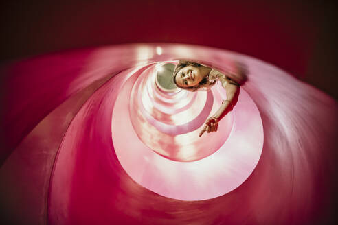 Smiling woman gesturing inside spiral structure - MJRF01003