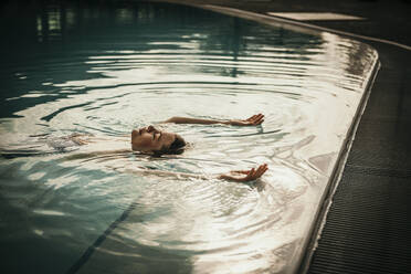 Frau mit erhobenen Armen im Schwimmbad schwimmend - MJRF01011