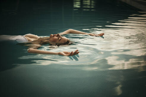 Woman with arms raised relaxing in swimming pool - MJRF01012