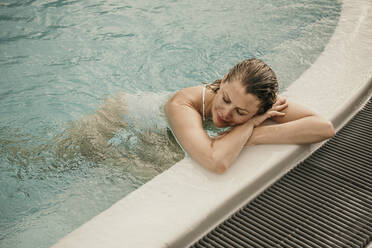 Woman with eyes closed resting in swimming pool - MJRF01015