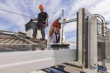 Ingenieure bei der Installation von Solarzellen auf dem Dach unter dem Himmel - JCCMF10057