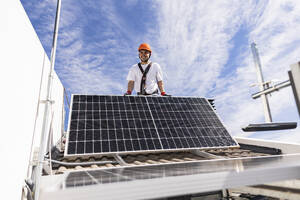 Smiling young engineer installing solar panels on roof - JCCMF10067