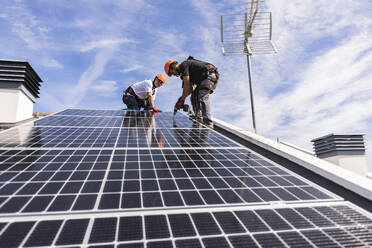 Ingenieure bei der Installation eines Solarpanels unter freiem Himmel an einem sonnigen Tag - JCCMF10069