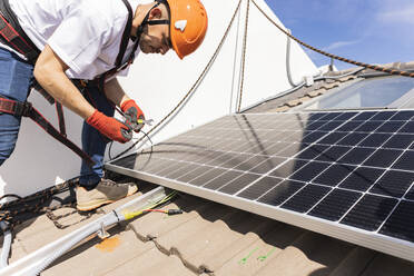 Junger Ingenieur mit Arbeitsgerät bei der Installation von Solarzellen - JCCMF10080