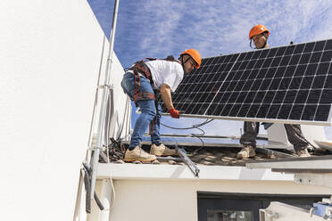 Techniker mit Kollege bei der Installation eines Solarpanels auf dem Dach - JCCMF10084