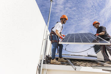 Junger Techniker mit Kollege bei der Installation von Solarzellen auf dem Dach - JCCMF10085