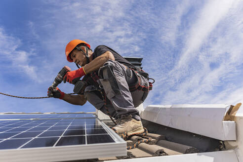Techniker bei der Arbeit mit einer Bohrmaschine und der Installation von Solarzellen auf dem Dach - JCCMF10089