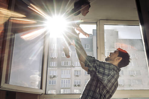 Vater spielt mit Sohn am Fenster an einem sonnigen Tag zu Hause - ANAF01127