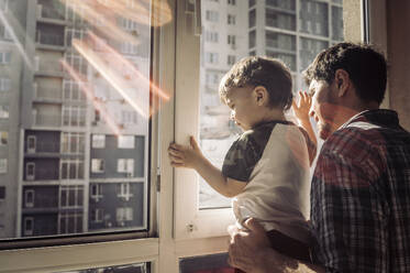 Vater und Sohn schauen zu Hause aus dem Fenster - ANAF01129