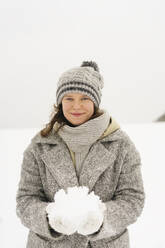 Lächelnde Frau mit Strickmütze, die Schnee hält - SEAF01835