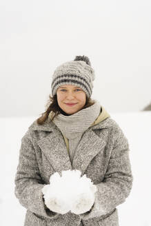 Smiling woman wearing knit hat holding snow - SEAF01835