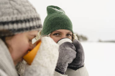 Friends wearing knit hats having coffee in winter - SEAF01854