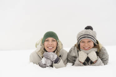 Glückliche Freunde mit Strickmützen und Handschuhen liegen im Schnee - SEAF01857