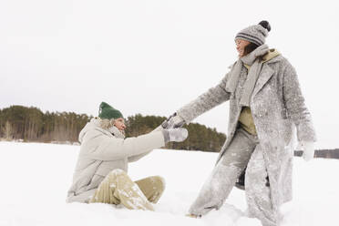 Glückliche Frau, die ihren Freund im Winter durch den Schnee zieht - SEAF01860