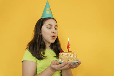 Mädchen bläst Kerze auf Geburtstagskuchen vor gelbem Hintergrund aus - OSF01482