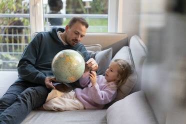 Vater und Tochter mit Globus sitzen auf dem Sofa zu Hause - MOEF04455