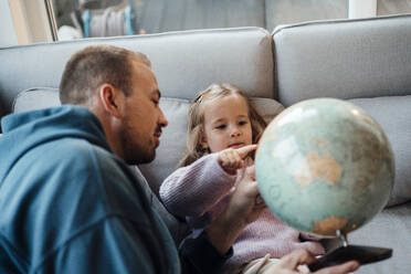 Daughter pointing at globe with father at home - MOEF04457