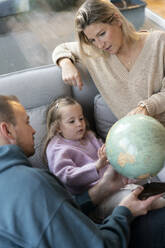 Daughter and parents sitting with globe on sofa at home - MOEF04458