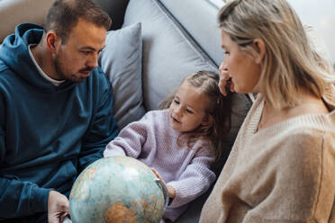 Tochter mit Eltern, die den Globus auf dem Sofa zu Hause betrachten - MOEF04460