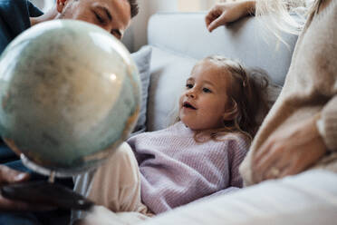 Tochter sitzt mit ihren Eltern im Wohnzimmer und betrachtet einen Globus - MOEF04462