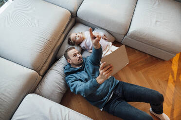 Vater hält Tablet-PC und gestikuliert mit seiner Tochter, die zu Hause liegt - MOEF04464