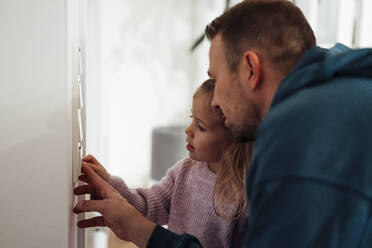Girl and father adjusting temperature on thermostat at home - MOEF04465