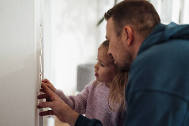 Mädchen und Vater stellen die Temperatur am Thermostat zu Hause ein - MOEF04465