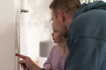 Father helping daughter in adjusting temperature on thermostat at home - MOEF04467