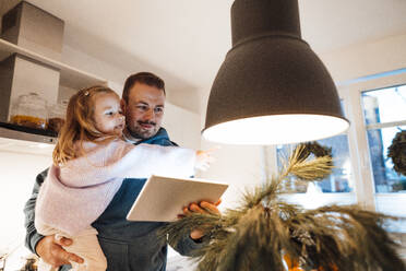 Father carrying daughter with tablet PC in kitchen - MOEF04474