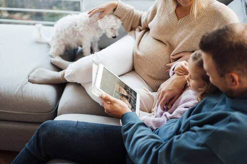 Mädchen führt Videogespräch mit Großvater über Tablet-PC, der bei den Eltern im Wohnzimmer sitzt - MOEF04481