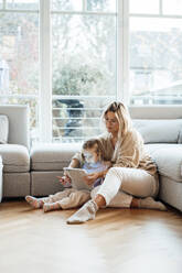 Woman sharing tablet PC with daughter sitting on floor in living room - MOEF04484